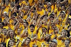 Football stands filled with ASU students, yelling and giving the Fork-em-Devils hand sign.